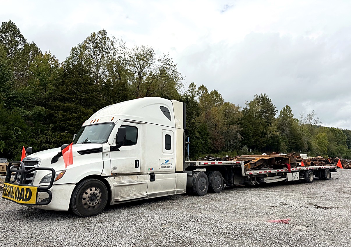 Oneway Group flatbed hauling an oversize steel load with OVERSIZE LOAD banner and orange flags