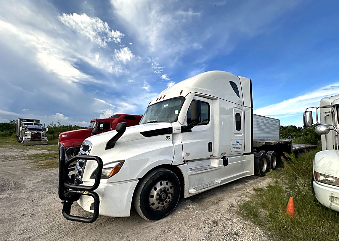 Oneway Group white Freightliner Cascadia unit 03 with brush guard and stepdeck trailer parked in a gravel yard